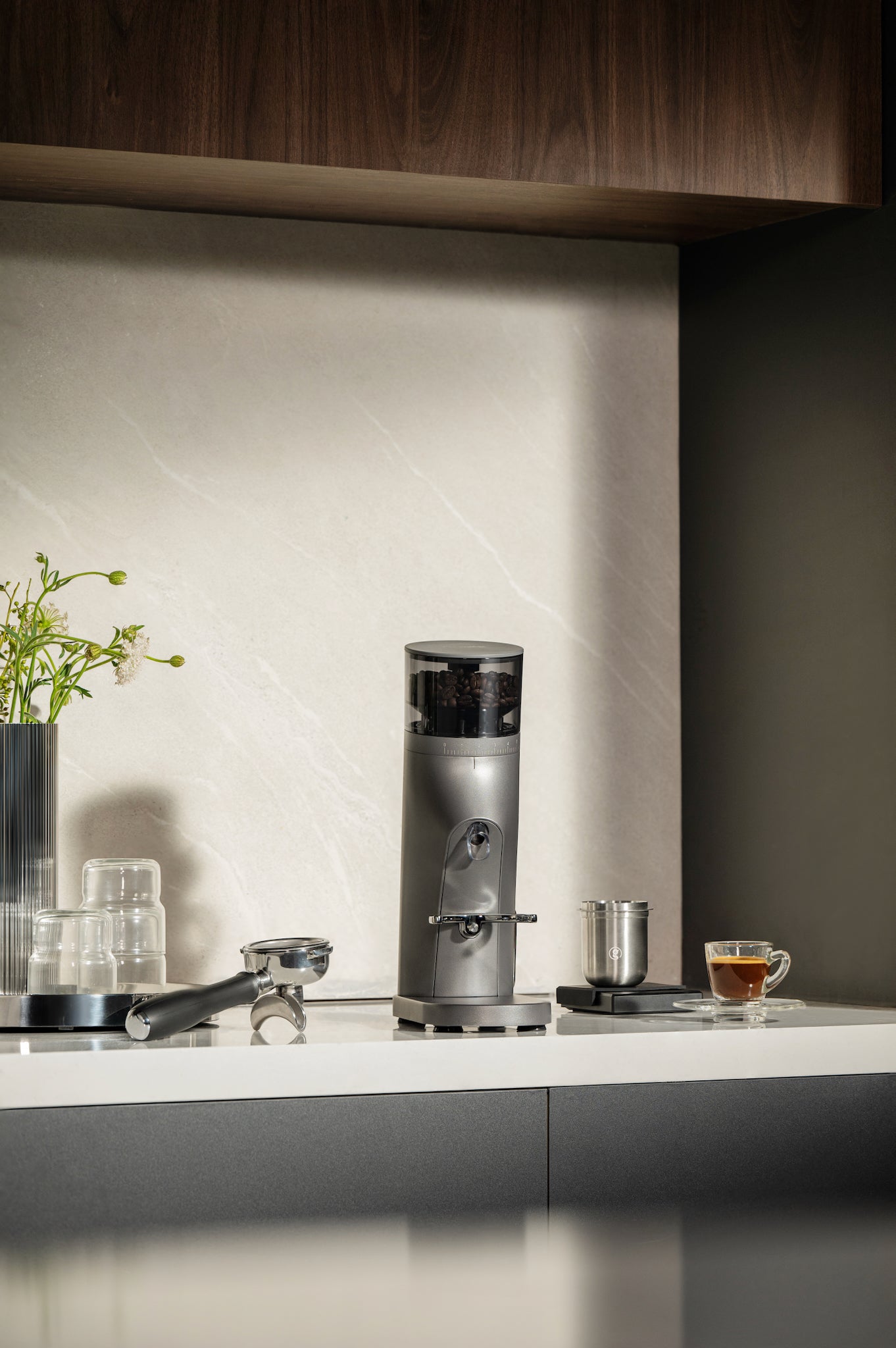 Gemilai G9010C Coffee grinder on a kitchen counter with a cup of coffee and a plant in the background.